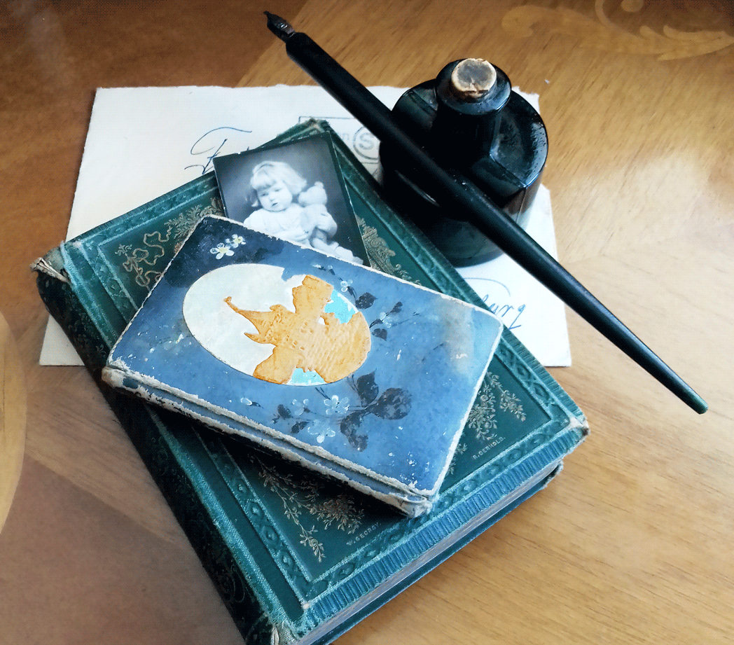 Stapel aus historischen Büchern, einer schwarzweiß Fotografie und einem Tintenfässchen mit Feder